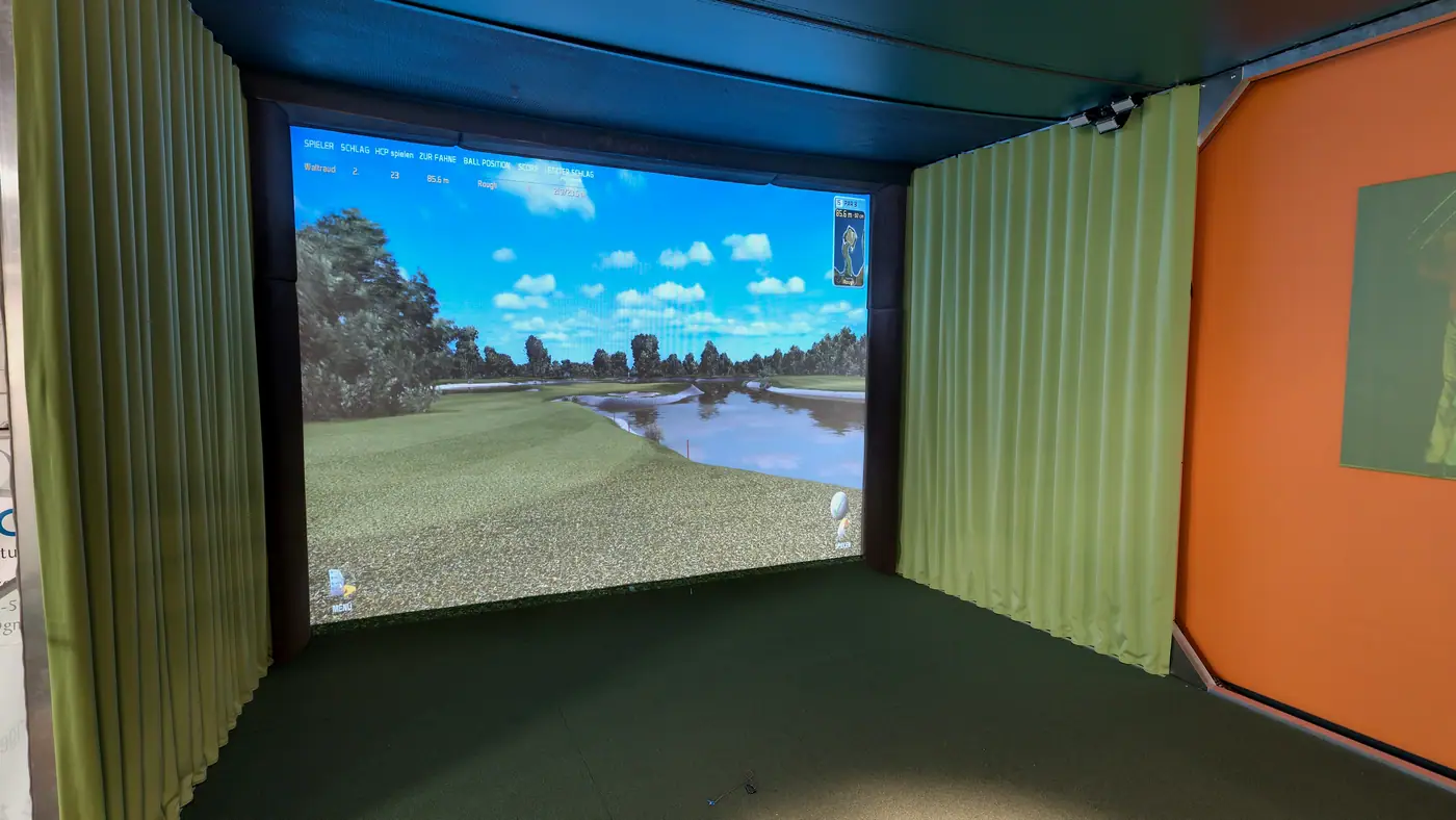 Der Golfsimulator im Obergeschoss: die Leinwand zeigt ein Fairway mit Teich, links und rechts grüne Vorhänge